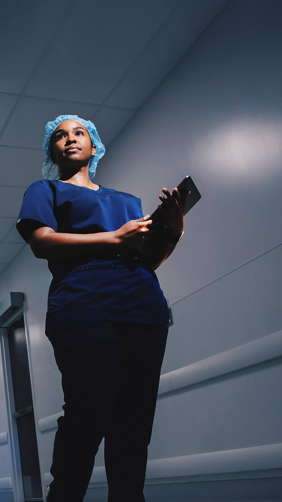 Nurse walking down a hospital corridor while holding a tablet.