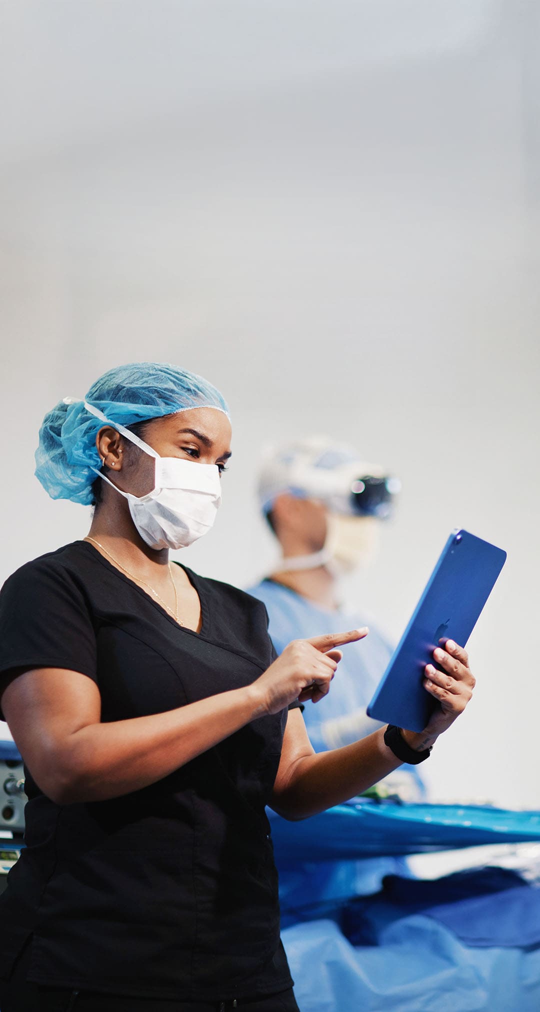 Nurse assisting surgeons during a procedure, using a Viewer X app on a tablet to access real-time updates.